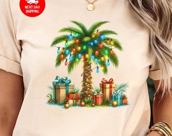 Könnte beinhalten: Beiges T-Shirt mit einem weihnachtlichen Palmen-Design. Der Baum ist mit bunten Lichtern geschmückt und von verpackten Geschenken umgeben. Das Design hat ein tropisches Weihnachtsthema.