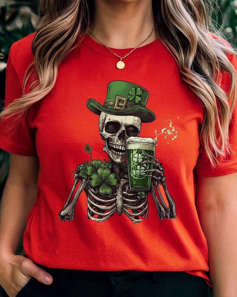 Puede incluir: Camiseta roja con un esqueleto vestido de duende verde, sosteniendo una jarra de cerveza verde. El esqueleto est&aacute; rodeado de tr&eacute;boles.
