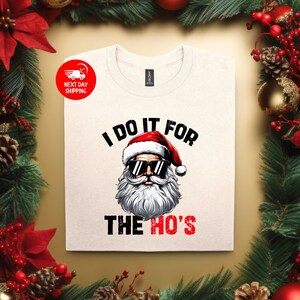 May include: White t-shirt featuring a Santa Claus wearing sunglasses and the text "I do it for the ho's".