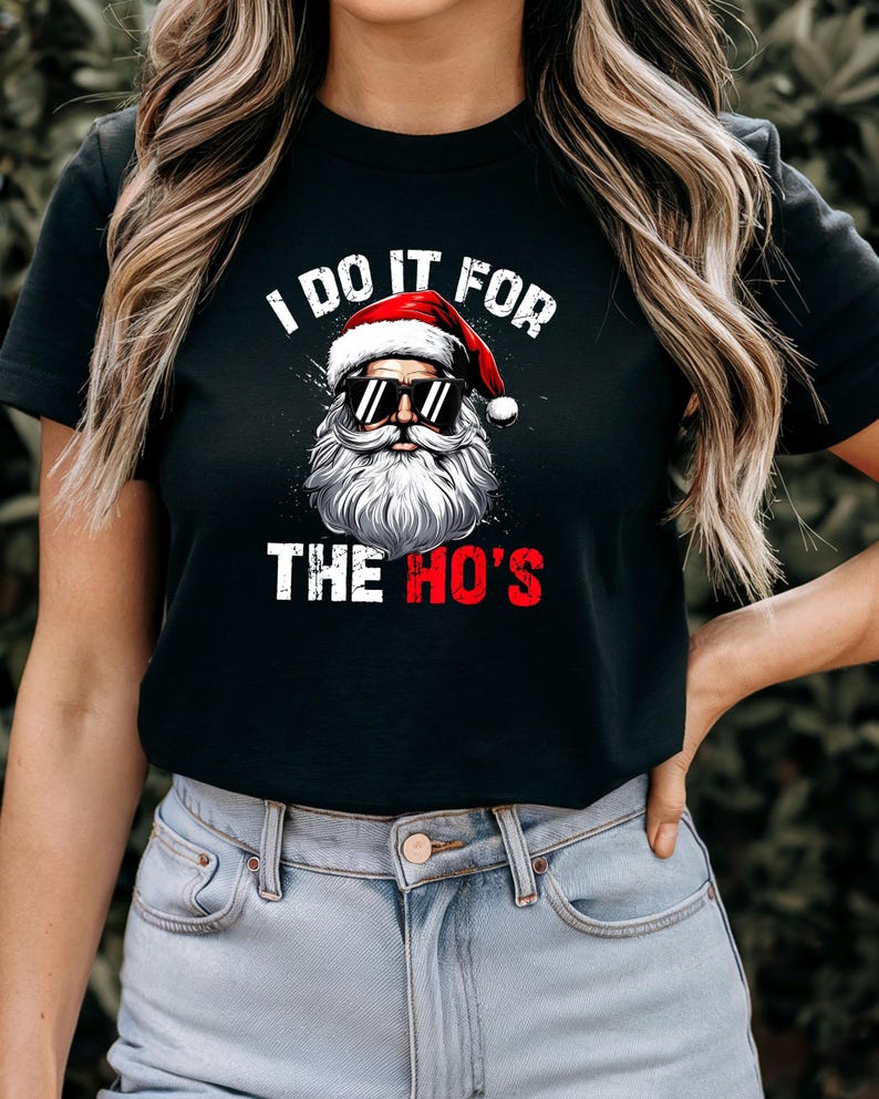 May include: Black short-sleeved t-shirt with a white graphic of Santa Claus wearing sunglasses and a red hat. The text "I do it for the ho's" is printed on the shirt.