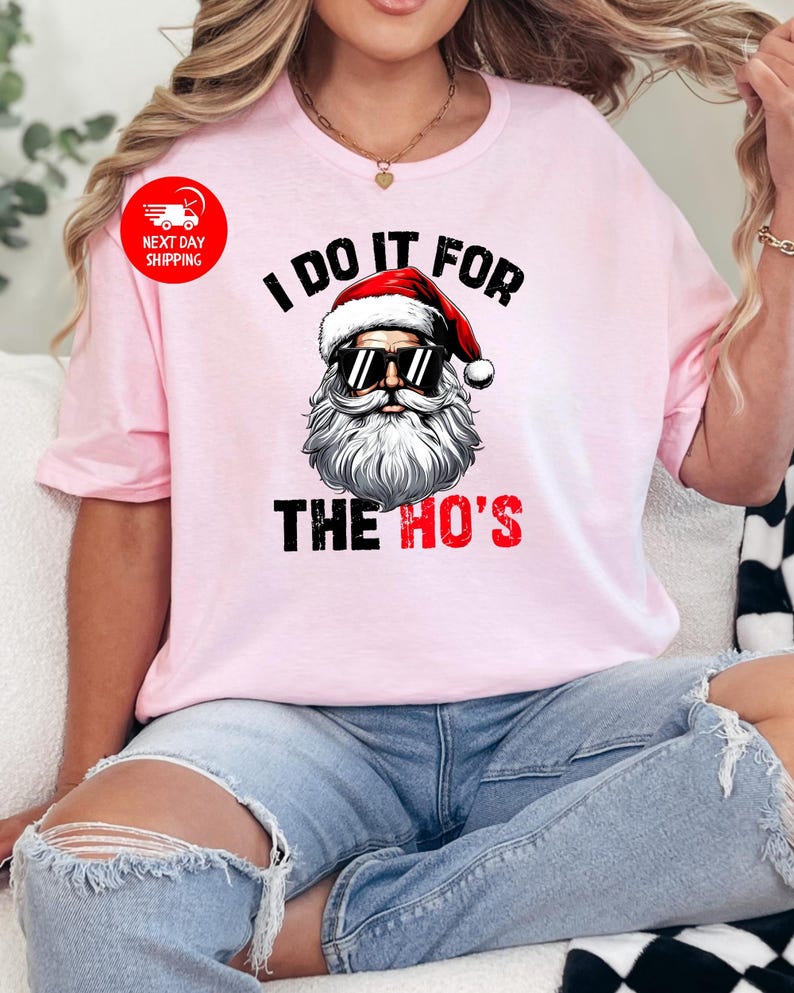May include: Pink t-shirt featuring a graphic of Santa Claus wearing sunglasses and the text "I do it for the ho's".