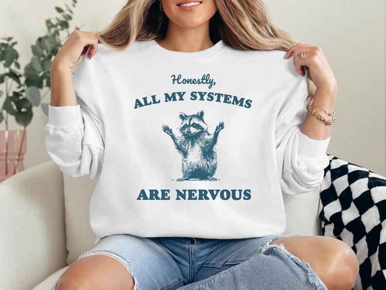 Puede incluir: Sudadera blanca con un gr&aacute;fico de mapache y el texto "Honestamente, todos mis sistemas est&aacute;n nerviosos".
