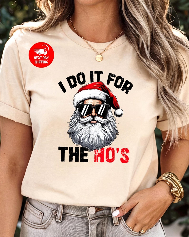May include: A beige t-shirt featuring a graphic of Santa Claus wearing sunglasses and the text "I do it for the ho's".