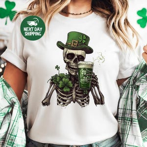 Puede incluir: Camiseta blanca con un esqueleto verde que lleva un sombrero de duende verde y sostiene una jarra de cerveza verde. El esqueleto est&aacute; rodeado de tr&eacute;boles verdes.