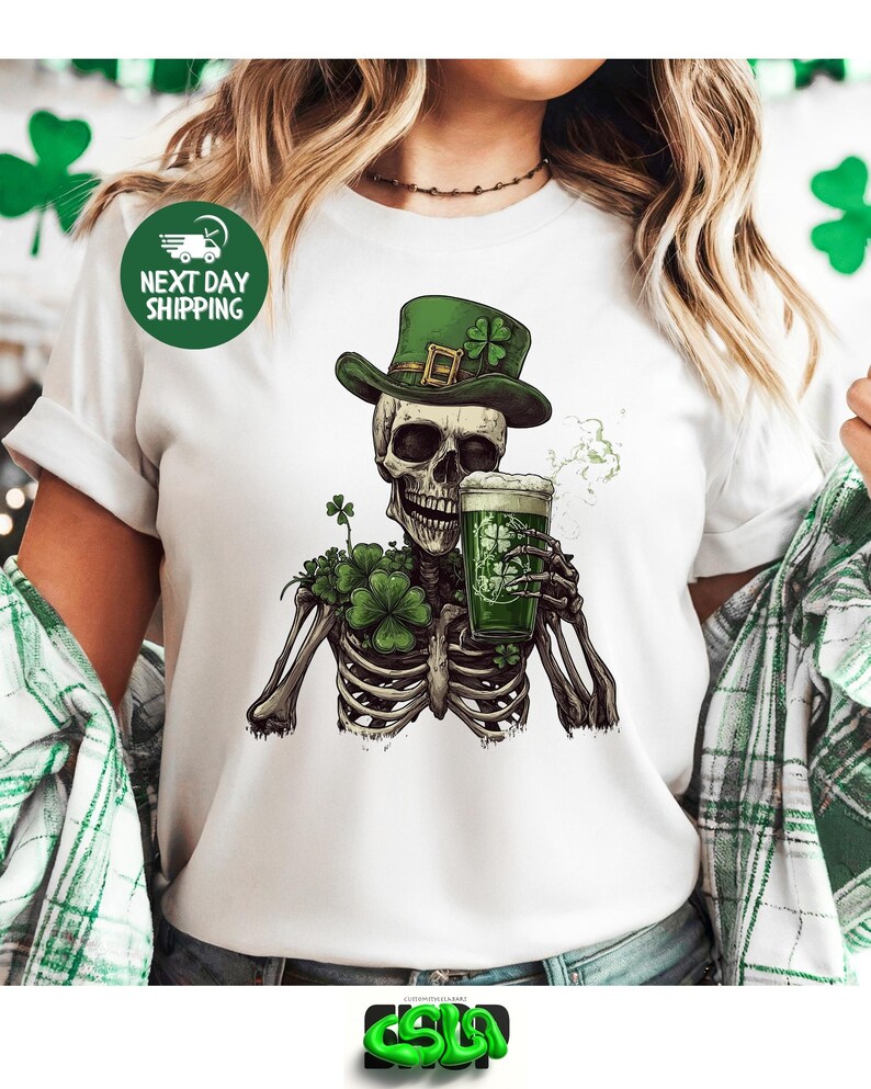 Puede incluir: Camiseta blanca con un esqueleto verde que lleva un sombrero de duende verde y sostiene una jarra de cerveza verde. El esqueleto est&aacute; rodeado de tr&eacute;boles verdes.