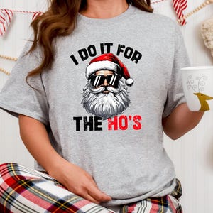 May include: A grey t-shirt with a graphic of Santa Claus wearing sunglasses and the text "I do it for the ho's".