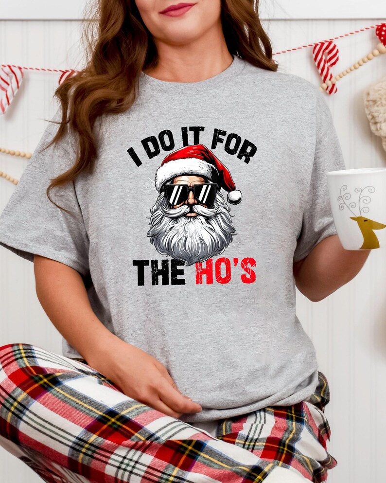 May include: A grey t-shirt with a graphic of Santa Claus wearing sunglasses and the text "I do it for the ho's".