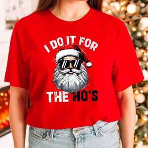 May include: Red t-shirt with a white graphic of Santa Claus wearing sunglasses and the text "I do it for the ho's".