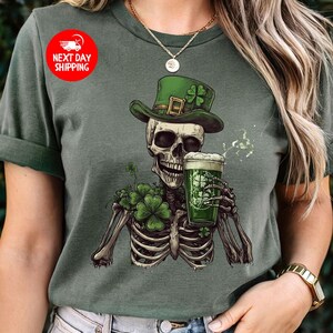 Puede incluir: Una camiseta verde con un esqueleto que lleva un sombrero verde de duende y sostiene una jarra de cerveza verde. El esqueleto est&aacute; rodeado de tr&eacute;boles verdes.