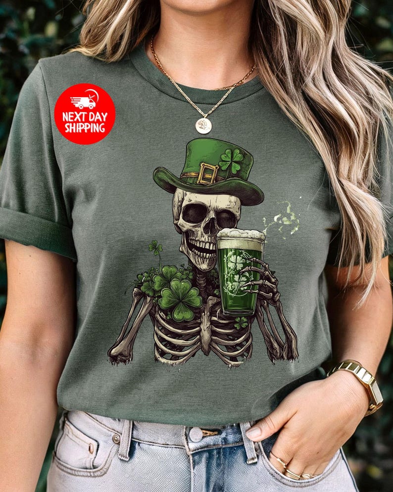 Puede incluir: Una camiseta verde con un esqueleto que lleva un sombrero verde de duende y sostiene una jarra de cerveza verde. El esqueleto est&aacute; rodeado de tr&eacute;boles verdes.