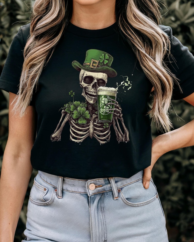 Puede incluir: Camiseta negra con un esqueleto verde que lleva un sombrero de duende verde y sostiene una jarra de cerveza verde. El esqueleto est&aacute; rodeado de tr&eacute;boles verdes.