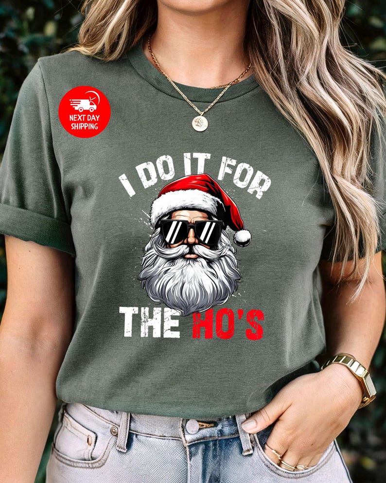 May include: Green t-shirt featuring a white graphic of Santa Claus wearing sunglasses and a white beard. The text "I do it for the ho's" is printed below the image.