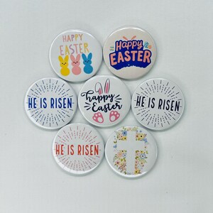 May include: Six round buttons with different Easter-themed designs. The buttons feature phrases like "Happy Easter", "He is Risen", and a cross with floral accents.