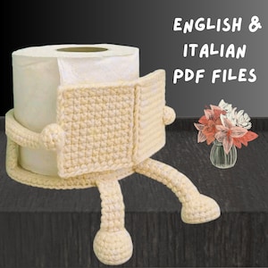 以下が含まれることがあります： 白いトイレットペーパーのロールが、腕と脚が付いたクリーム色の編み物カバーに包まれています。「ENGLISH & ITALIAN PDF FILES」の文字が白で表示されています。右側には小さな花瓶に入った花があります。