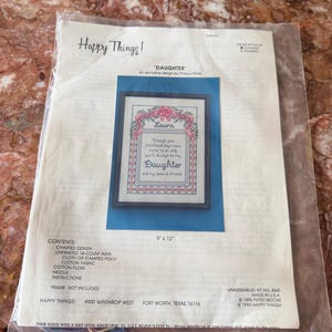 May include: A Happy Things cross stitch kit titled Daughter, featuring a design with pink ribbons, floral accents, and the text: Though your childhood days have come to an end, you'll always be my Daughter and my special friend. Includes 9" x 12" dimensions.