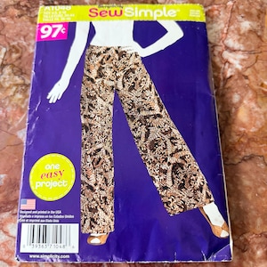 May include: A Simplicity Sew Simple sewing pattern envelope A1048 featuring a graphic illustration of wide-leg pants with a brown, black, and white fern leaf pattern. The purple packaging includes the text one easy project and a barcode.