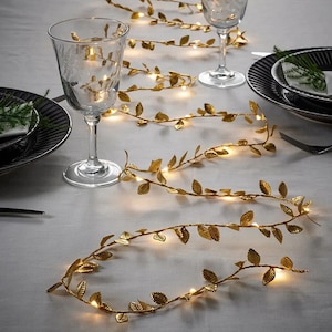 May include: Gold leaf garland with warm white LED lights. The garland is made of metal leaves and wire, and is ideal for adding a touch of sparkle to any space.