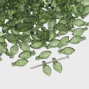May include: A collection of translucent green glass leaf beads. The beads are detailed with leaf veins and have a small loop at the top for stringing. A metal pin is included for attaching the beads. Ideal for jewelry making and craft projects.