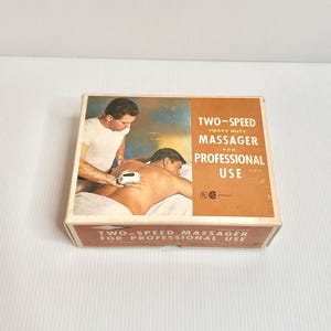 Könnte beinhalten: Vintage Box für ein Zwei-Gang-Hochleistungsmassagegerät für den professionellen Gebrauch. Die Box zeigt ein Bild einer Person, die eine Massage erhält. Der Text auf der Box lautet "ZWEI-GESCHWINDIGKEITEN MASSAGEGERÄT FÜR DEN PROFESSIONELLEN GEBRAUCH."
