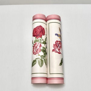 May include: Two rolled wallpaper samples with floral designs. One features a large red rose with green leaves, the other a red and purple tulip. Both have pink accents and a cream background.