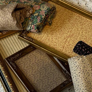 May include: Four ornate gold picture frames with different patterned fabric inserts. The frames are arranged in a pile, with the largest frame on top and the smallest frame on the bottom.