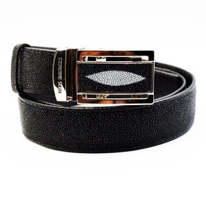 Peut inclure: Une ceinture en cuir noir avec une boucle argentée. La boucle est ornée d'un incrustation de peau de raie blanche et le texte "GENUINE SKIN" est gravé sur le côté.