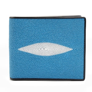 May include: A bi-fold wallet with a textured, light blue exterior and a white, oval-shaped design in the center. The wallet has black trim and a square shape. The surface has a pattern of small, closely spaced dots.