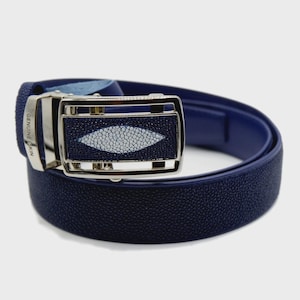 Op de afbeelding: Een marineblauwe riem met een leren band met textuur en een zilveren gesp. De gesp heeft een rechthoekige inleg met een wit en grijs roggenpatroon. De woorden "GENUINE SKIN" staan op de gesp.