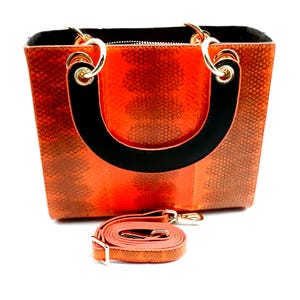 Può includere: Borsa a mano arancione con manico nero e tracolla rimovibile. La borsa ha un motivo a pelle di serpente.
