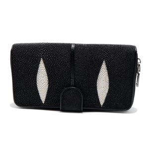 May include: A rectangular black wallet featuring a textured surface with two prominent, elongated white diamond-shaped inlays. The wallet includes a central vertical strip and a small rounded tab closure at the bottom edge, with a silver zipper pull.
