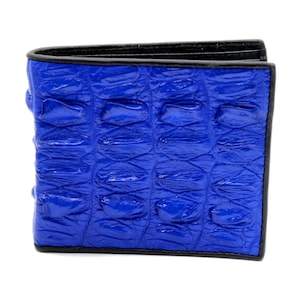Puede incluir: Cartera azul brillante de dos pliegues, con un patrón texturizado similar a la piel de cocodrilo. La cartera tiene un borde negro y parece estar hecha de cuero. Un accesorio clásico y práctico.