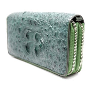 May include: A rectangular wallet with a textured, teal-coloured exterior featuring a raised, embossed pattern. The wallet has two separate compartments, each secured with a silver-toned metal zip and a green fabric lining along the edges.