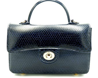 Könnte beinhalten: Eine marineblaue Handtasche mit einem strukturierten Wabenmuster. Die Tasche hat einen oberen Griff, einen goldfarbenen Verschluss und kleine goldene Füße. Das Design ist strukturiert und elegant, passend für verschiedene Anlässe.