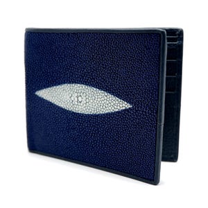 Puede incluir: Una cartera plegable hecha de cuero de raya azul marino oscuro, con un distintivo parche blanco de forma ovalada alargada en el centro con una superficie texturizada y granulada. La cartera tiene ranuras para tarjetas visibles en el panel lateral.