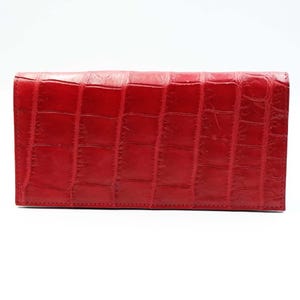 May include: A red, rectangular wallet with a textured, crocodile-like pattern. The wallet is made of a smooth material and has a stitched border. The wallet is closed and appears to be empty.