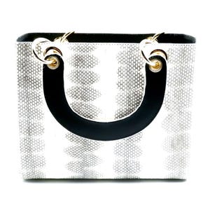 May include: A white handbag with a black leather handle and gold hardware. The bag has a snakeskin pattern.