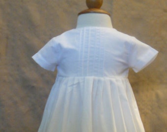 May include: A white christening gown with a pleated skirt and short sleeves.
