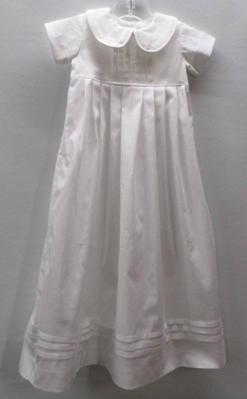 May include: White christening gown with a peter pan collar and short sleeves. The gown has pleats in the front and a scalloped hem.