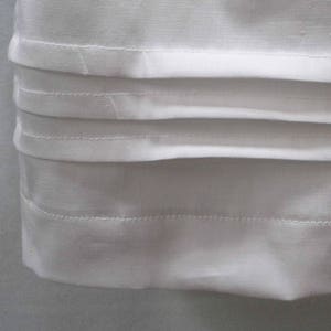 May include: White fabric with multiple rows of stitching along the bottom edge. The fabric is folded over to create a clean, finished edge.