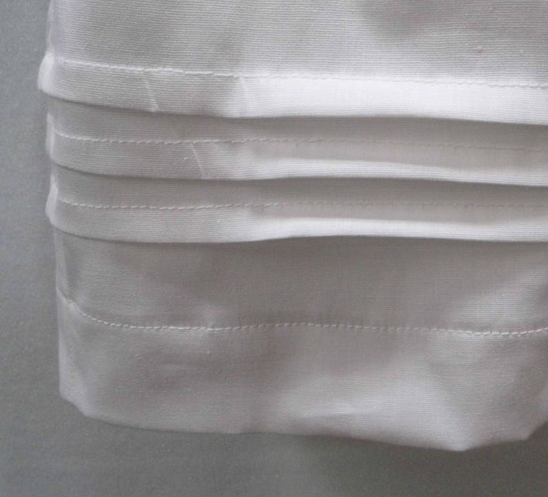 May include: White fabric with multiple rows of stitching along the bottom edge. The fabric is folded over to create a clean, finished edge.