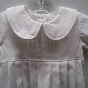May include: A white baby outfit with a peter pan collar and pleated skirt.
