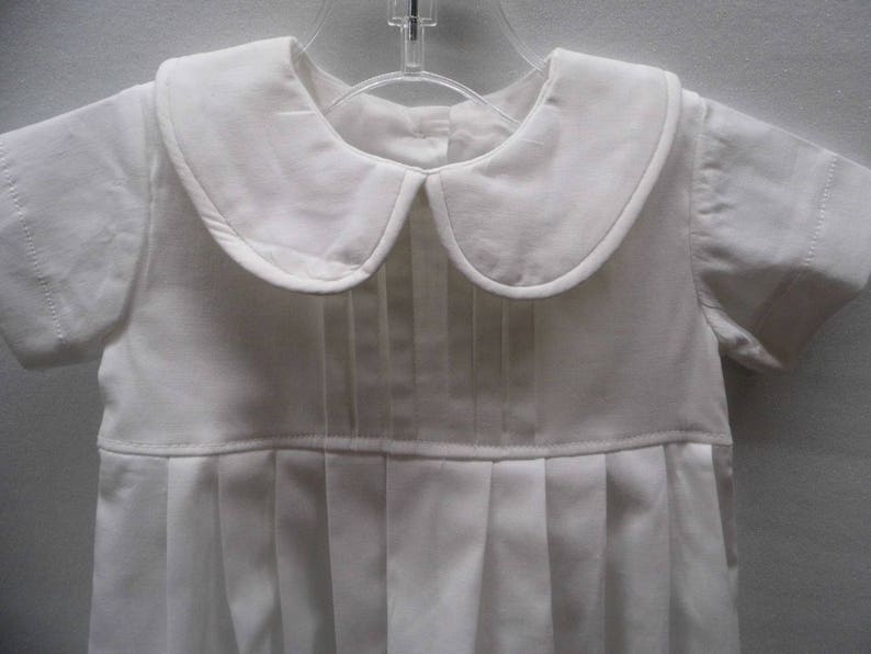 May include: A white baby outfit with a peter pan collar and pleated skirt.