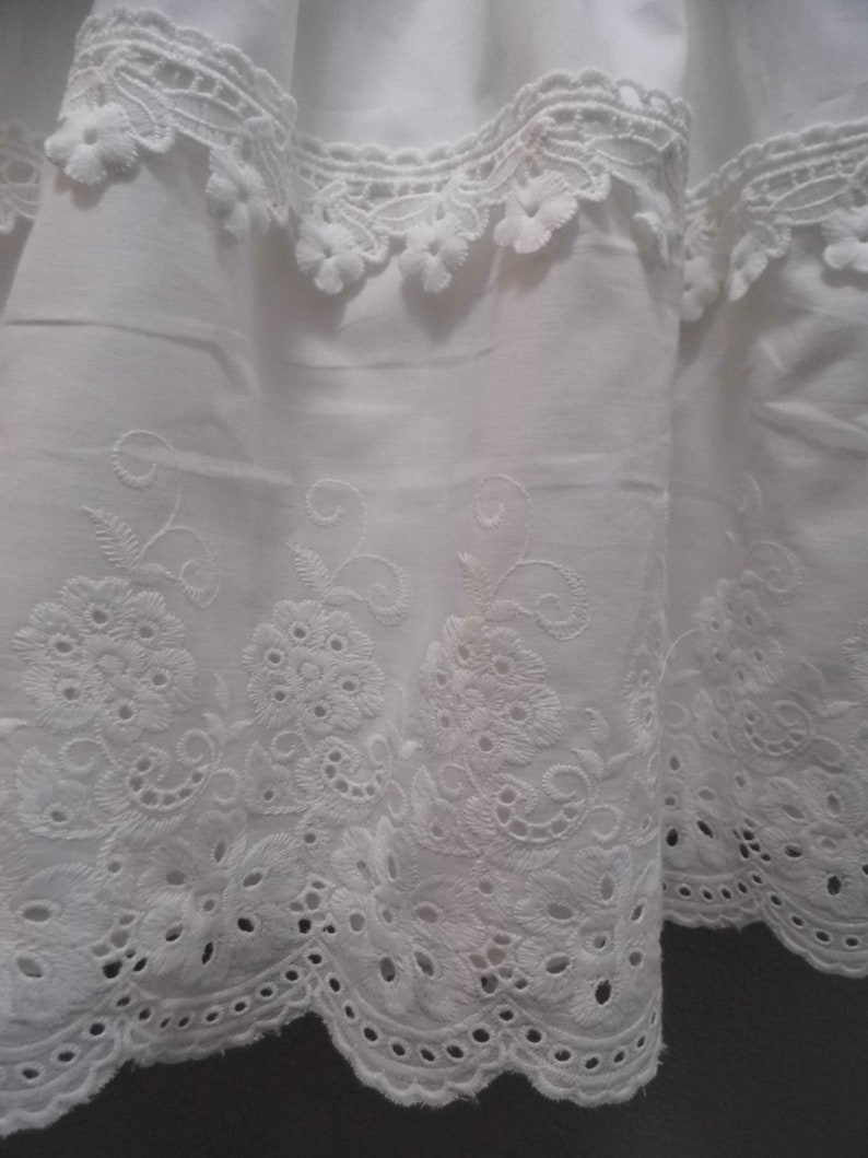 Puede incluir: Tela de algod&oacute;n blanca con un delicado ribete de encaje bordado. El encaje presenta un borde festoneado y un dise&ntilde;o floral.