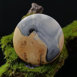 May include: A round, polished stone with a swirling pattern of gray, brown, and white. The stone has a natural, organic look.