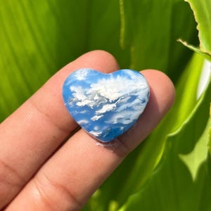 Könnte beinhalten: Ein herzförmiger Edelstein mit einer glatten, polierten Oberfläche, einer leuchtend blauen Grundfarbe und komplizierten, feinen weißen Einschlüssen, die wie Wolken an einem klaren Himmel aussehen und ein natürliches, detailliertes Muster bilden.