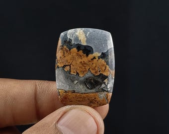 May include: A rectangular, multi-colored, polished stone cabochon with a layered pattern of black, brown, white, and gray. The stone has a natural, organic look.