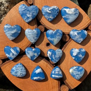 Könnte beinhalten: Eine Sammlung herzförmiger und dreieckiger blauer Edelsteine mit weißen wolkenartigen Mustern. Die Steine sind auf einer Holzoberfläche angeordnet und zeigen ihre einzigartige Farbe und ihr Design. Die Edelsteine sind ein leuchtendes Blau.