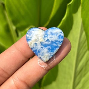 Könnte beinhalten: Ein herzförmiger Stein mit einer leuchtend blauen Grundfarbe und komplizierten, wolkenartigen weißen Mustern auf der Oberfläche. Der polierte Edelstein weist eine glatte, glänzende Textur und eine ausgeprägte Herzsilhouette mit abgerundeter Oberseite auf.