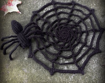 May include: A black crocheted spider and web, the spider is sitting on the edge of the web.
