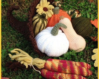May include: A crocheted cornucopia filled with crocheted pumpkins, gourds, and a sunflower. The cornucopia is brown and the pumpkins are white, orange, and green. There are also crocheted corn stalks.